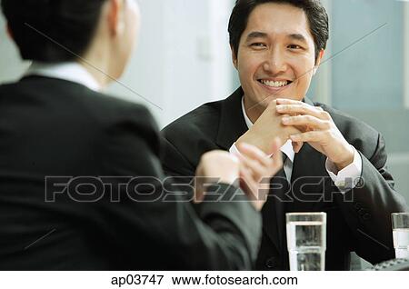 Stock Photo - Businessman smiling, at woman in front of him. Fotosearch