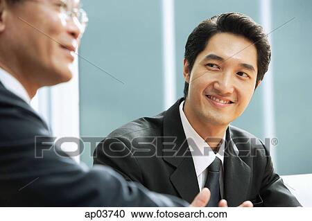 Businessman smiling, looking at man next to him View Large Photo Image Stock Image - Businessman smiling, looking at man next to him . Fotosearch
