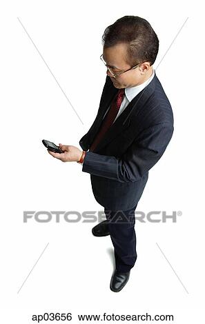 Stock Photograph - Businessman standing, looking at mobile phone. Fotosearch