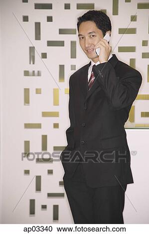 Stock Image - Businessman using mobile phone, looking at camera. Fotosearch