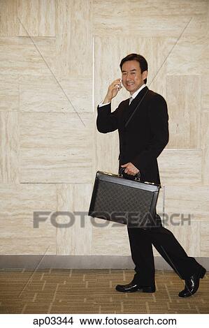 Businessman with briefcase, using mobile phone, smiling at camera View Large Photo Image Picture - Businessman with briefcase, using mobile phone, smiling at camera . Fotosearch