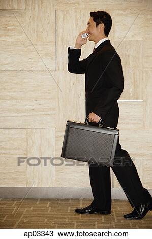 Stock Image - Businessman with briefcase, using mobile phone . Fotosearch