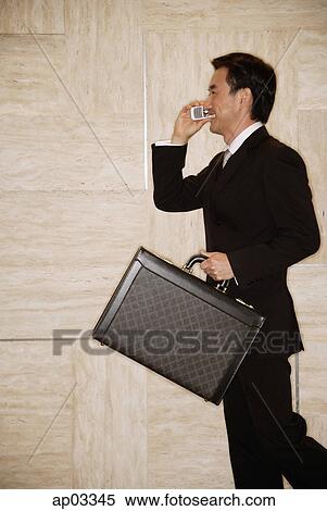 Stock Photography - Businessman with briefcase, using mobile phone, smiling . Fotosearch