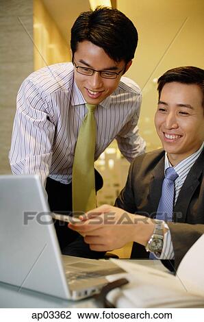 Stock Image - Businessmen working together, looking at laptop . Fotosearch