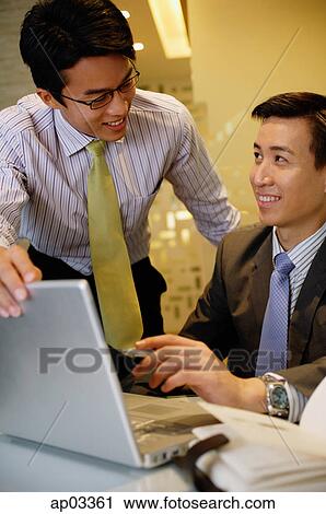 Stock Image - Businessmen working together, using laptop. Fotosearch