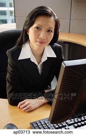 Businesswoman sitting at desk, looking at camera View Large Photo Image Stock Image - Businesswoman sitting at desk, looking at camera . Fotosearch
