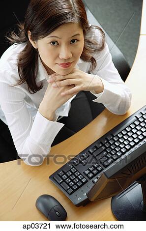 Businesswoman sitting in office cubicle, hands on chin, looking up at camera View Large Photo Image Stock Image - Businesswoman sitting in office cubicle, hands on chin, looking up at camera. Fotosearch