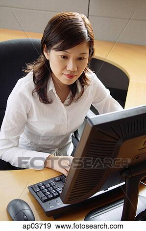 Businesswoman sitting in office cubicle, looking at computer View Large Photo Image Stock Photo - Businesswoman sitting in office cubicle, looking at computer. Fotosearch