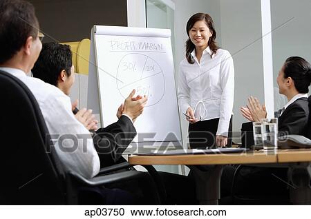 Businesswoman standing next to flipchart, colleagues sitting and clapping View Large Photo Image Stock Image - Businesswoman standing next to flipchart, colleagues sitting and clapping . Fotosearch