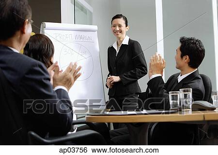 Stock Photograph - Businesswoman standing next to flipchart, other executives clapping . Fotosearch