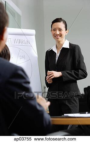 Businesswoman standing next to flipchart, smiling at colleagues View Large Photo Image Stock Photography - Businesswoman standing next to flipchart, smiling at colleagues. Fotosearch
