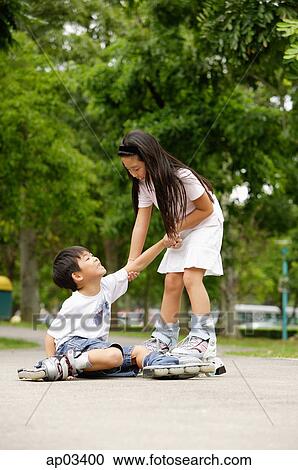 Stock Image - Children skating, boy on the ground, girl pulling him up . Fotosearch