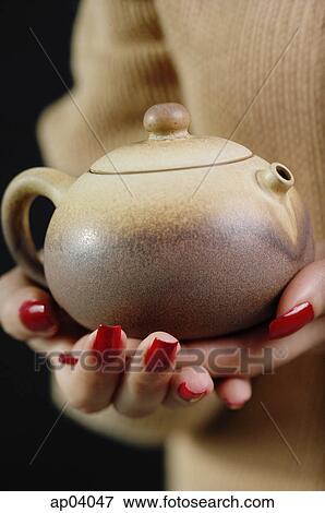 Stock Photo - Close up of womans hands holding tea pot. Fotosearch