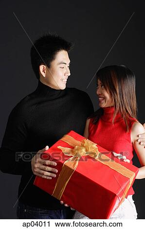 Couple holding gift, looking at each other View Large Photo Image Stock Image - Couple holding gift, looking at each other. Fotosearch