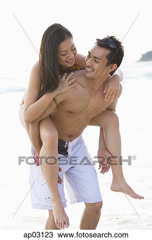 Couple on beach, woman riding piggyback on man View Large Photo Image Stock Image - Couple on beach, woman riding piggyback on man. Fotosearch