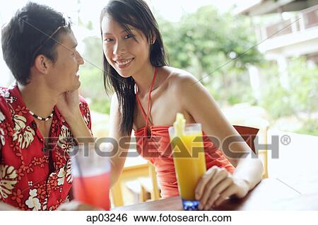 Stock Photograph - Couple sitting face to face, man looking at woman, woman smiling at camera . Fotosearch
