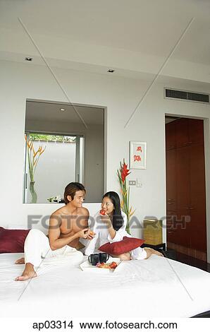 Picture - Couple sitting on bed, eating breakfast. Fotosearch
