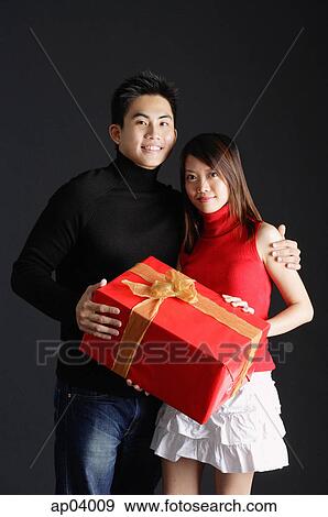 Stock Photo - Couple standing side by side, holding gift. Fotosearch