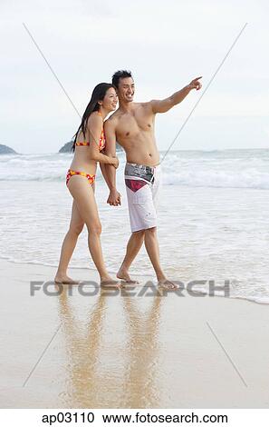 Couple walking on beach, holding hands, man pointing to the distance View Large Photo Image Stock Image - Couple walking on beach, holding hands, man pointing to the distance . Fotosearch