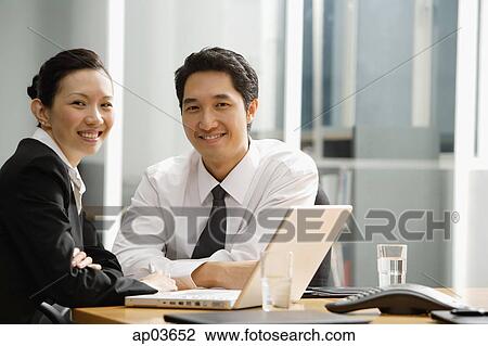 Executives at table with laptop, smiling at camera View Large Photo Image Stock Image - Executives at table with laptop, smiling at camera. Fotosearch