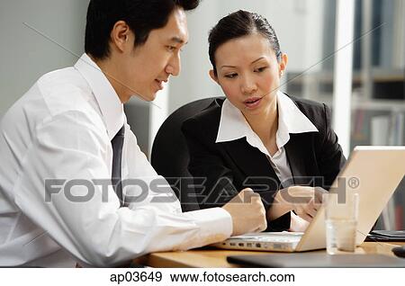 Stock Photo - Executives sitting at table, looking at laptop. Fotosearch