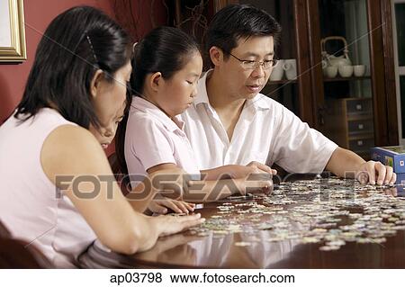 Family of four fixing jigsaw puzzle on coffee table View Large Photo Image Stock Photo - Family of four fixing jigsaw puzzle on coffee table. Fotosearch