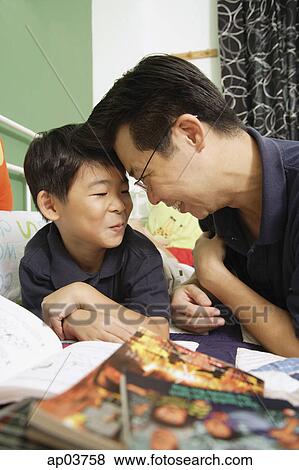 Stock Photo - Father and son sitting side by side on bed, making faces . Fotosearch