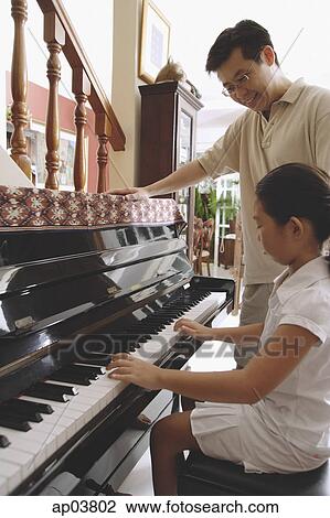 Stock Image - Father watching daughter playing the piano . Fotosearch