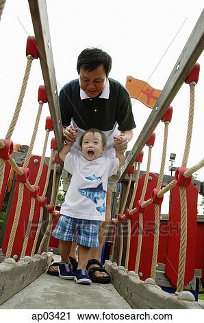 Stock Image - Father with young son in playground, walking on bridge. Fotosearch