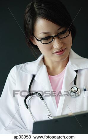 Stock Photo - Female doctor looking at clipboard. Fotosearch