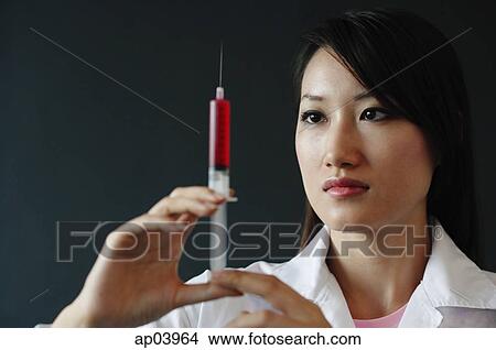 Female doctor looking at syringe, serious expression View Large Photo Image Picture - Female doctor looking at syringe, serious expression . Fotosearch