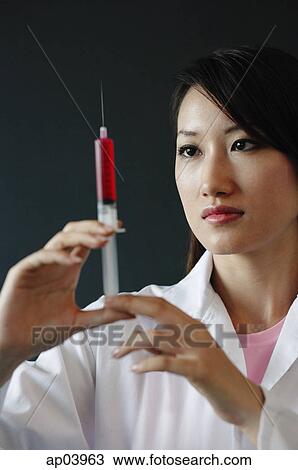 Stock Image - Female doctor looking at syringe . Fotosearch