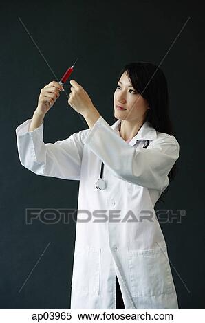 Female doctor standing, looking at syringe View Large Photo Image Stock Photography - Female doctor standing, looking at syringe. Fotosearch