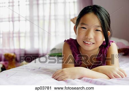 Girl in bedroom, lying on bed, smiling at camera View Large Photo Image Stock Image - Girl in bedroom, lying on bed, smiling at camera . Fotosearch