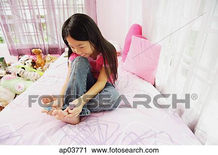 Stock Image - Girl in bedroom, painting toenails. Fotosearch