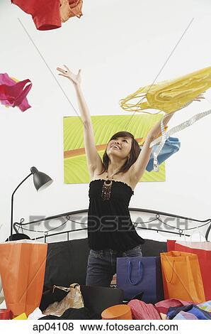 Stock Photo - Girl kneeling on bed, throwing clothes in the air . Fotosearch