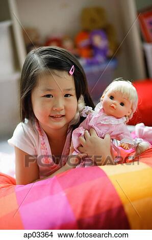 Girl lying on bed, holding a doll View Large Photo Image Picture - Girl lying on bed, holding a doll . Fotosearch