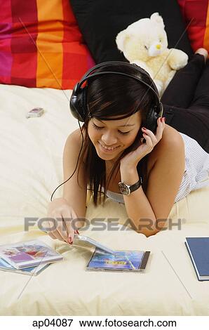 Stock Photo - Girl lying on bed, listening to headphones . Fotosearch