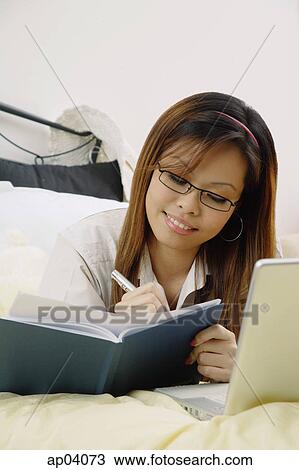 Girl lying on bed, writing in book View Large Photo Image Stock Image - Girl lying on bed, writing in book. Fotosearch
