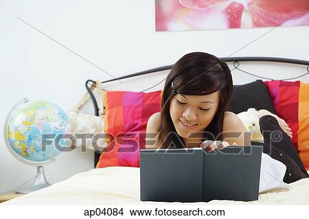 Picture - Girl lying on bed, writing in diary. Fotosearch