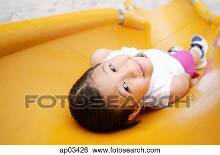 Stock Photograph - Girl lying on slide, smiling at camera . Fotosearch
