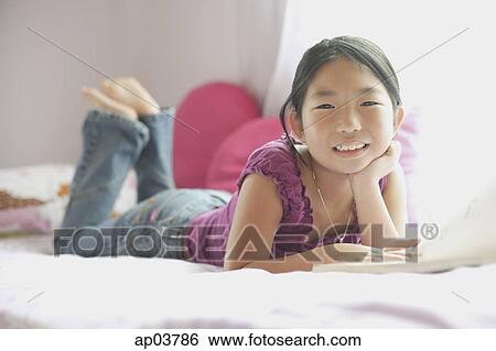 Stock Photograph - Girl on bed, hands on chin, smiling at camera . Fotosearch