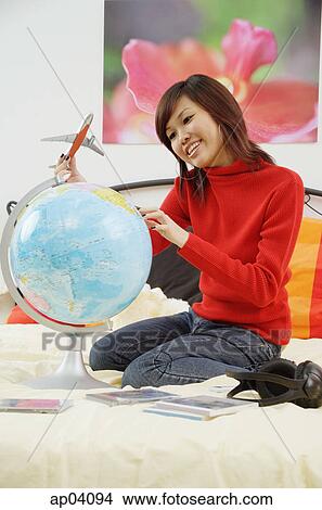 Picture - Girl on bed, holding toy airplane and looking at globe. Fotosearch