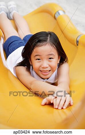Picture - Girl on yellow slide, smiling at camera . Fotosearch