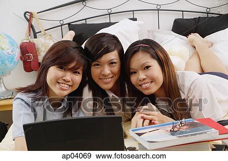 Stock Photo - Girls in school uniform lying side by side on bed, smiling at camera. Fotosearch