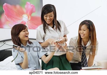 Girls in school uniform, sitting on bed, looking at mobile phones View Large Photo Image Stock Image - Girls in school uniform, sitting on bed, looking at mobile phones . Fotosearch