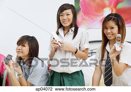 Girls in school uniform, sitting on bed, holding mobile phones View Large Photo Image Stock Image - Girls in school uniform, sitting on bed, holding mobile phones . Fotosearch