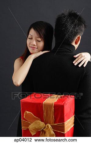 Man holding gift behind his back, woman embracing him View Large Photo Image Stock Image - Man holding gift behind his back, woman embracing him. Fotosearch