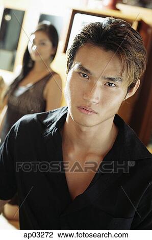 Stock Image - Man looking at camera, woman in the background. Fotosearch