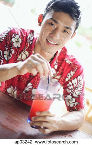 Stock Image - Man wearing floral shirt, holding a drink, looking at camera . Fotosearch